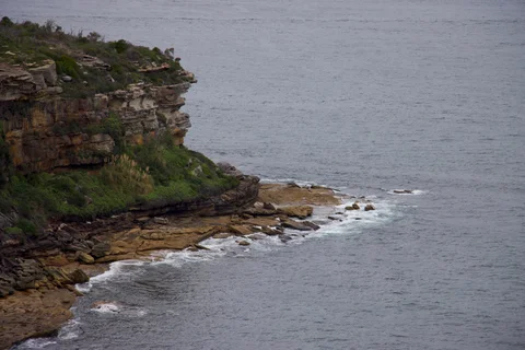 A rocky cliff overlooks the ocean, with a small island in the water.