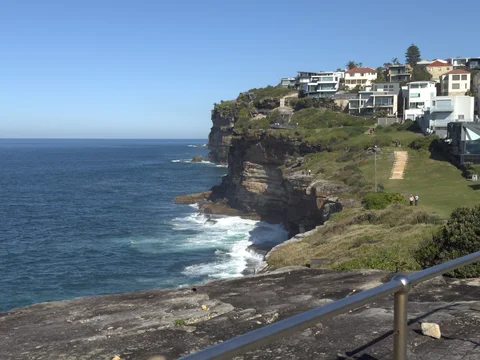 A scenic view of a cliff overlooking the ocean with houses and a road below.