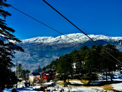 A snowy mountain with a ski lift and a ski lodge in the foreground.