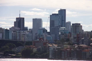  The image depicts a bustling cityscape with a large body of water in the foreground. The city is filled with tall buildings, including a prominent skyscraper, which dominates the skyline. The buildings are a mix of various colors, creating a vibrant and lively atmosphere. The water appears to be calm, reflecting the city's beauty and tranquility. The scene captures the essence of a modern, urban environment, with the city's architectural marvels and the serene waterfront creating a harmonious balance between nature and urban development.