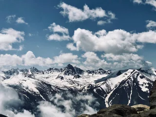  The image captures a breathtaking view of a snow-covered mountain range with clouds surrounding it. The mountains are majestic and towering, creating a sense of awe and wonder. The sky above the mountains is a deep shade of blue, contrasting beautifully with the white snow. The clouds in the scene add a sense of depth and dimension to the landscape, making it appear more expansive and serene. This picturesque scene evokes feelings of tranquility and appreciation for the beauty of nature.