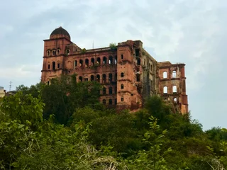 The image features a large, old, and abandoned building with a red brick exterior. The building has a distinctive clock tower, which stands out against the red brick backdrop. The clock is visible on the side of the tower, adding a sense of history and architectural interest to the scene. The overall mood of the image is one of decay and abandonment, as the building appears to be in a state of disrepair. The presence of the clock tower and the red brick exterior give the scene a sense of nostalgia and a connection to the past.